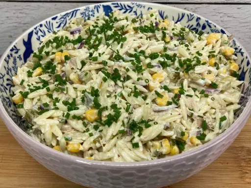 Pyszna sałatka z tuńczykiem i makaronem orzo, z kukurydzą i szczypiorkiem, w ozdobnej misce.