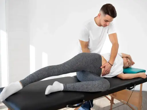 Fizjoterapeuta wykonuje terapię manualną, pomagając pacjentce w rozluźnieniu biodra. To właśnie terapia manualna co to jest – technika leczenia bólu i dysfunkcji.