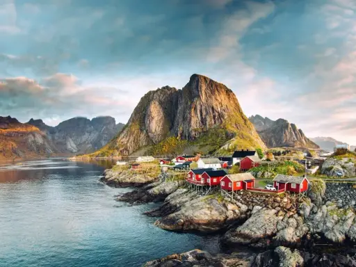 Röda fiskestugor vid en vik, med dramatiska berg i bakgrunden. En idyllisk vy som visar var ligger Lofoten.