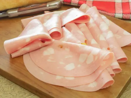 Fette di salame rosa, come in attesa di un lieto evento, disposte su un tagliere di legno.