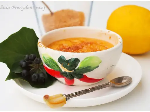 Słodka, karmelizowana crema catalana w ozdobnej miseczce, obok cytryna i jagody.