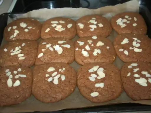 Douze biscuits faits maison, parfaits pour une recette speculoos, garnis d'amandes effilées sur une plaque de cuisson.