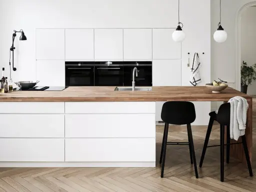 Un plan de travail en bois chaleureux contraste avec les meubles de cuisine blancs. Quelle couleur de plan de travail pour une cuisine blanche ? Le bois est une option parfaite.