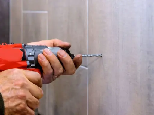 Man usa una broca para azulejo con un taladro para hacer un agujero en una pared de azulejos.