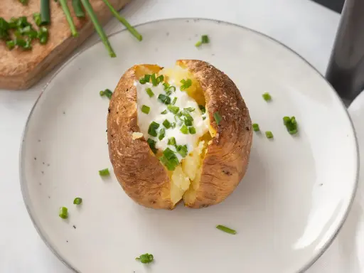 Patatas asadas en freidora de aire, crujientes por fuera, tiernas por dentro, coronadas con crema agria y cebollino fresco.