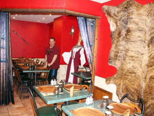 Un homme se tient dans un restaurant moyen âge décoré d'une peau d'ours et d'une épée.