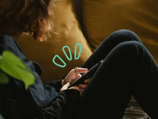 Une personne aux cheveux roux utilise son smartphone, symbolisant quelles peuvent être les principales conséquences de la cyberdépendance : isolement, anxiété, perte de temps.