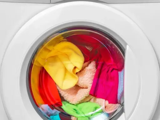 Bunte Wäsche, darunter ein gelber und ein grüner Schwamm, wartet in der Waschmaschine auf das schwamm waschen.
