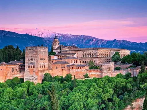 Alhambra w Granadzie na tle ośnieżonych gór i różowego nieba o zachodzie słońca.