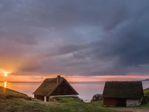 Två gamla hus med halmtak vid havet i Skåne Tranås. Solnedgången färgar himlen orange och lila.