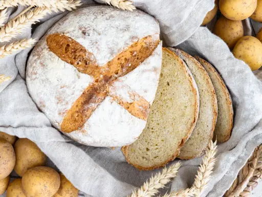 Frisch gebackenes Kartoffelbrot, aufgeschnitten und mit Kartoffeln und Weizenähren dekoriert. Ein tolles Rezept für Kartoffelbrot!