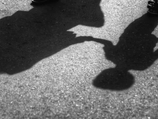 Dwie postacie, dorosła i dziecko, trzymają się za ręce. Cienie na asfalcie sugerują, że to może być dowód na reinkarnację, gdzie dusze odnajdują się w kolejnych wcieleniach.