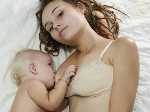 Mama z dredami karmi piersią niemowlę. To piękny moment bliskości, choć nie jest to karmienie piersią 10 latka.
