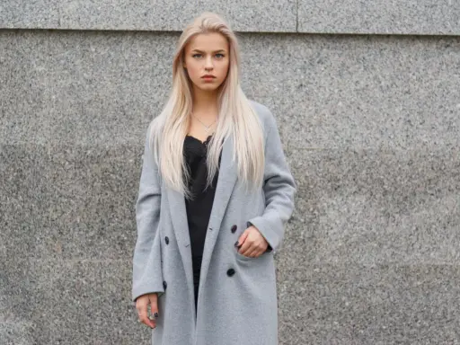 Blondynka w szarym płaszczu i czarnej koronkowej bluzce. Czerń to klasyczny wybór, jaki kolor pasuje do szarego ubrania, dodając elegancji.