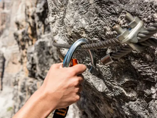 Dłoń zapina karabinek do stalowej liny na via ferrata. Bezpieczeństwo podczas wspinaczki.