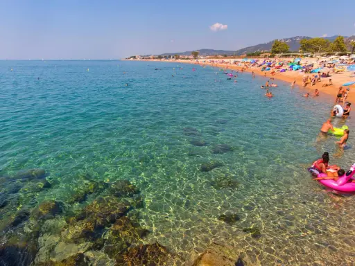 Spiaggia affollata a Santa Susanna, Spagna, con persone che nuotano e si rilassano in un mare cristallino.