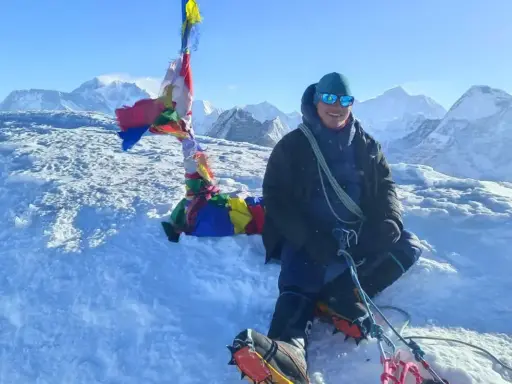 Szczęśliwy alpinista na szczycie Mera Peak, otoczony śniegiem i modlitewnymi flagami, z majestatycznymi górami w tle.