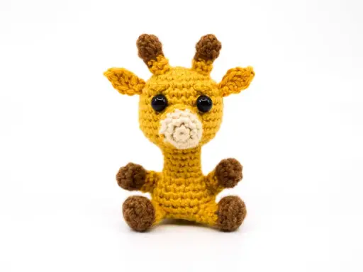 Tierna jirafa amigurumi amarilla, sentada con sus patitas marrones. Sus ojos negros y hocico beige le dan un aspecto adorable.