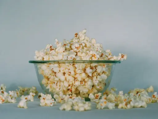 Góra popcornu w szklanej misce, rozsypane ziarna wokół. Ile popcorn kcal?