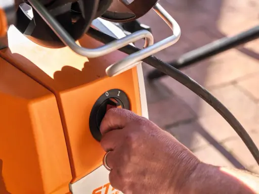 Hand dreht Schalter am orangefarbenen Hochdruckreiniger. Vorbereitung zum Anschluss an den Wasserhahn.