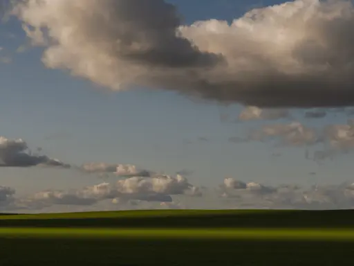 Zachód słońca nad zielonym polem, rzucającym długi cień. Chmury na niebie tworzą ciekawe fotografie.