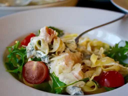 En krämig laxpasta med spenat, körsbärstomater och ruccola. En gaffel lyfter upp en bit av den läckra pastan.