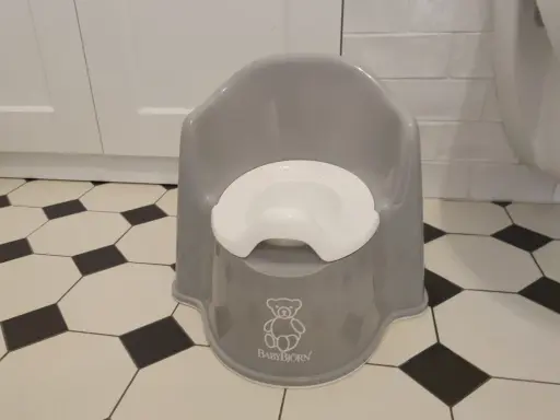 Szary nocnik BabyBjörn z białym siedziskiem, symbolizujący nowy etap w procesie odpieluchowania.