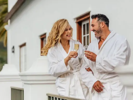 Para relaksu w hotelach spa w Polsce. Uśmiechnięta para w szlafrokach wznosi toasty szampanem na balkonie.