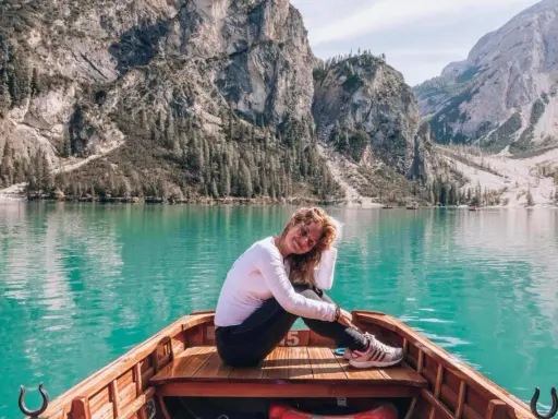 Kobieta w łodzi na turkusowym jeziorze w Dolomitach, w tle góry i las.