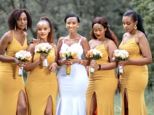 Cinco mujeres con vestidos amarillos y la novia con vestido blanco, todas con ramos de flores. Ellas son la dama de honor y caballero de honor.
