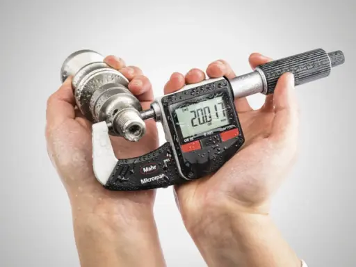 Manos sostienen un micrometro digital Mahr Micromar, midiendo una pieza metálica. La pantalla muestra 200.17 mm.