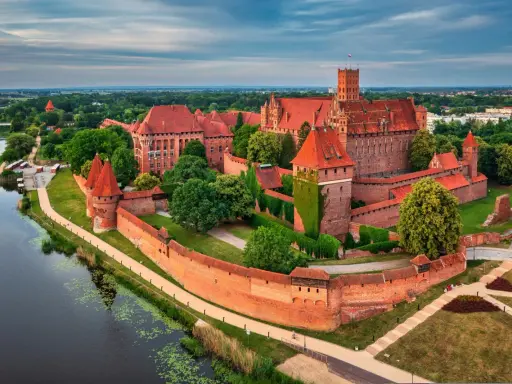 Potężny zamek w Malborku, jedna z największych atrakcji Polski, otoczony murami obronnymi i rzeką Nogat.