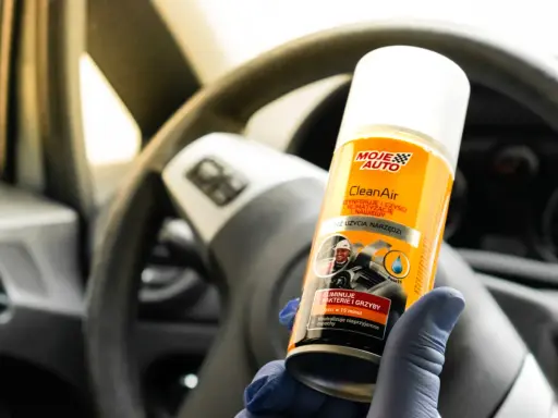 Rękawiczka w niebieskiej rękawiczce trzyma puszkę Moje Auto CleanAir do czyszczenia klimatyzacji.