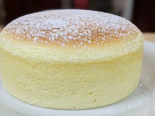 Un délicieux cheesecake japonais, léger et aérien, saupoudré de sucre glace sur une assiette blanche.