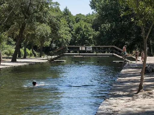 Un día soleado en las piscinas naturales de La Codosera. Personas disfrutan del agua fresca, una nada mientras otras pasean por la orilla.