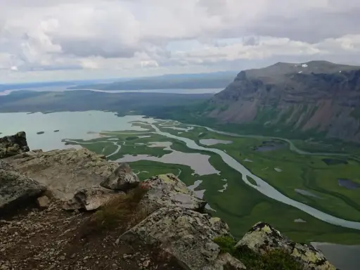 Vacker utsikt över Rapadalen med Skierfe i bakgrunden. En slingrande flod flyter genom ett grönt landskap med sjöar.