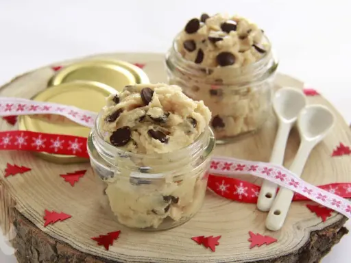 Två glasburkar fyllda med chokladbitsdeg, perfekt för ett enkelt cookie dough recept. Dekorerat med julband och små granar.