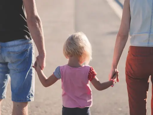 Rodzina idzie razem, trzymając się za ręce. Dziecko z blond włosami, w kolorowej bluzce, między rodzicami. Może to być obraz rodziny, która radzi sobie z zaburzeniami zachowania ICD 10.