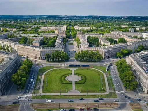 Plac Centralny w Nowej Hucie z socrealistyczną zabudową, zielonymi skwerami i torami tramwajowymi.