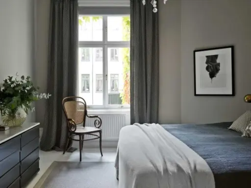 Sovrum med en säng, en stol och en byrå. Konst av Sofia Wallenstam på väggen.