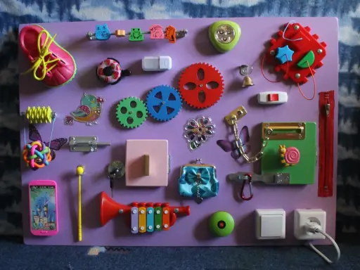 Lavagna sensoriale fai da te con scarpa, ingranaggi, campanello, lucchetto e altri elementi per stimolare i bambini. Perfetta per giochi montessori 2 anni fai da te.