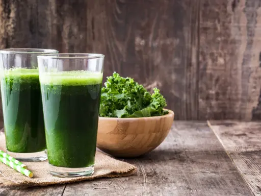 Dwa szklanki zielonego smoothie, miska jarmużu i słomki. Idealne na śniadanie zgodne z dietą sirtuinową.
