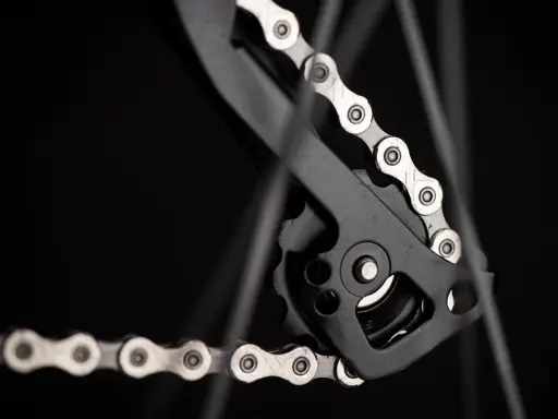 Jak dobrać łańcuch do roweru? Detal przerzutki tylnej z metalowym łańcuchem rowerowym na czarnym tle.