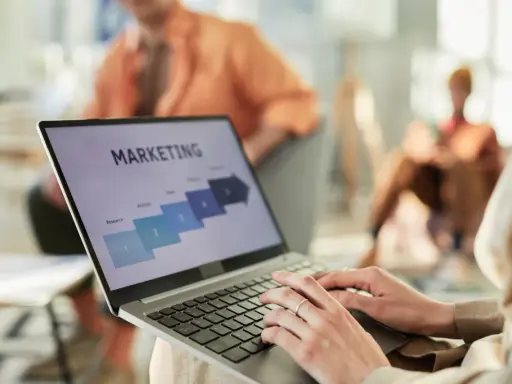 Osoba pracuje na laptopie z prezentacją "MARKETING". Widoczne etapy: Research, Analysis, Sales. Idealne do studiów zarządzanie i marketing.