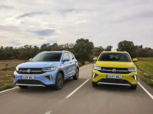 Un Volkswagen T-Cross azul y un T-Roc amarillo circulan por una carretera rural.