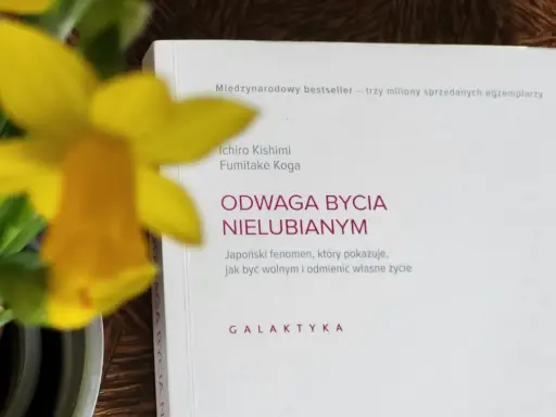Żółty narcyz obok książki "Odwaga bycia nielubianym". Odkryj sztukę bycia sobą i wolności.