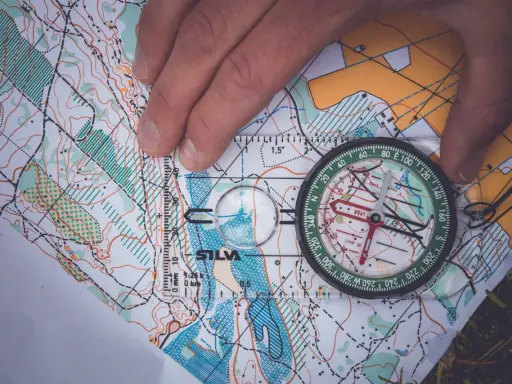 En hand håller en kompass över en karta, vilket visar hur fungerar en kompass för orientering.