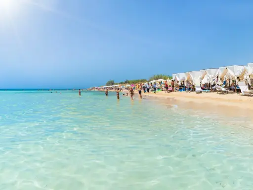 Spiaggia affollata con lettini e ombrelloni bianchi, gente che nuota e prende il sole. Un'immagine perfetta delle località balneari Puglia.