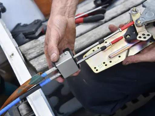 Main d'un mécanicien démontant le boîtier de commande d'un bateau, révélant les câbles et le mécanisme.