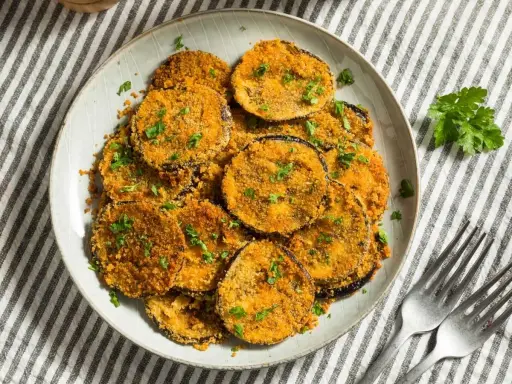 Plato de berenjenas rebozadas, doradas y crujientes, espolvoreadas con perejil fresco.